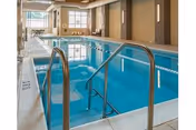 Indoor swimming pool with stainless handrails, lap lanes, and windows at the far end.