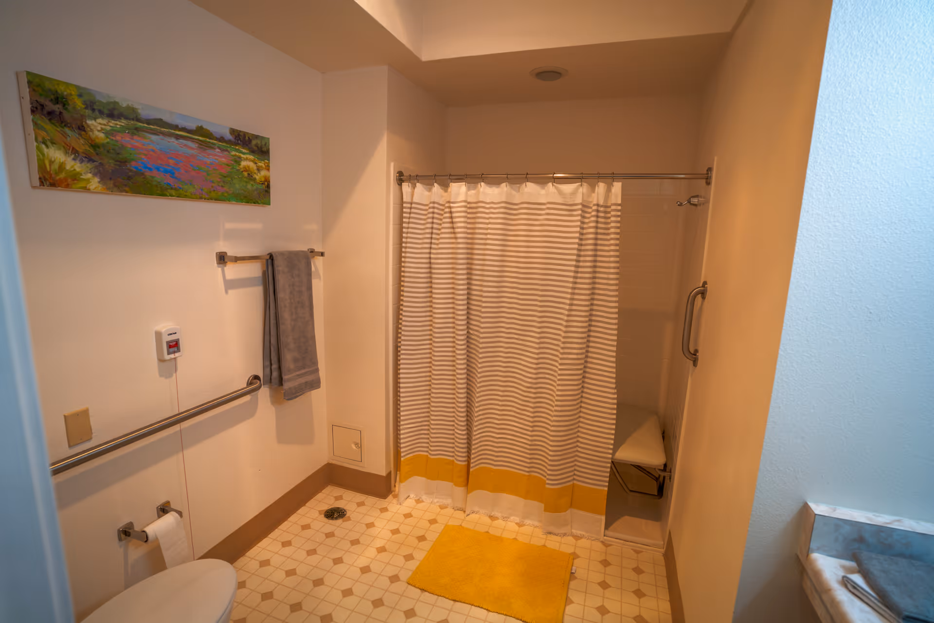 Accessible bathroom with a striped shower curtain, grab bars, toilet, towel, and a yellow bath mat.