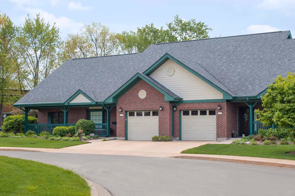 Brick single-story residential building with green trim, two garage doors, front porches, and a landscaped lawn.