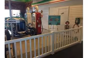 Indoor display area featuring vintage gas pumps and a classic gas station setup behind a white picket fence, with a 'No Smoking' sign visible on the fence.