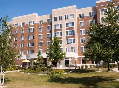 Exterior view of a multi-story brick senior living building with landscaped lawn and trees