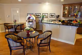 Interior view of a dining area with round tables and chairs, a counter with food and decorative items, a jukebox, and framed pictures on the wall.