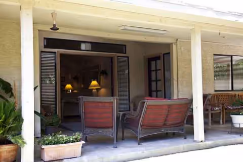 Covered patio with wicker seating, potted plants, and open French doors to an interior lounge.