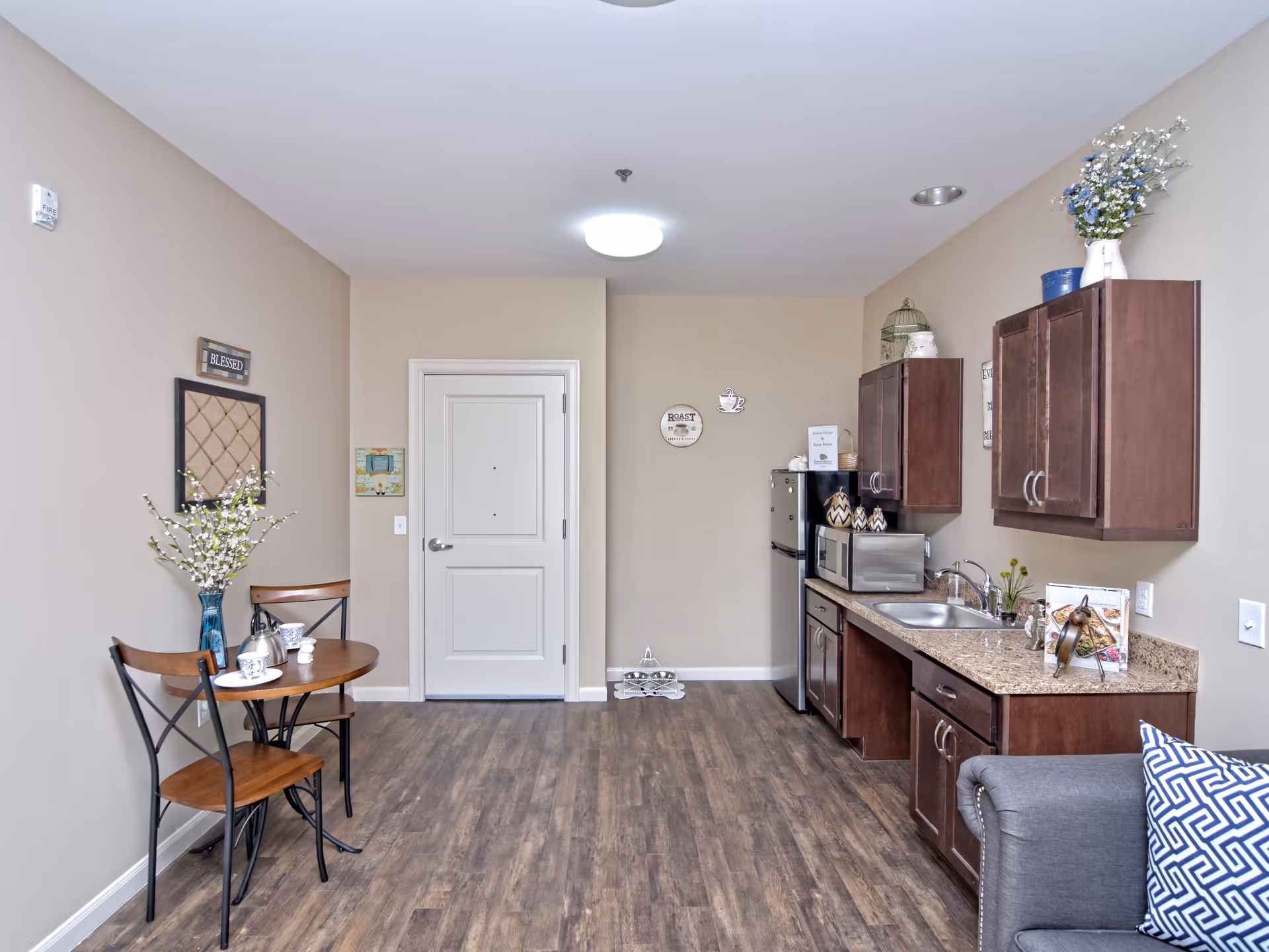 Compact apartment interior featuring a kitchenette with dark cabinets, a small two-person dining table, and a couch.