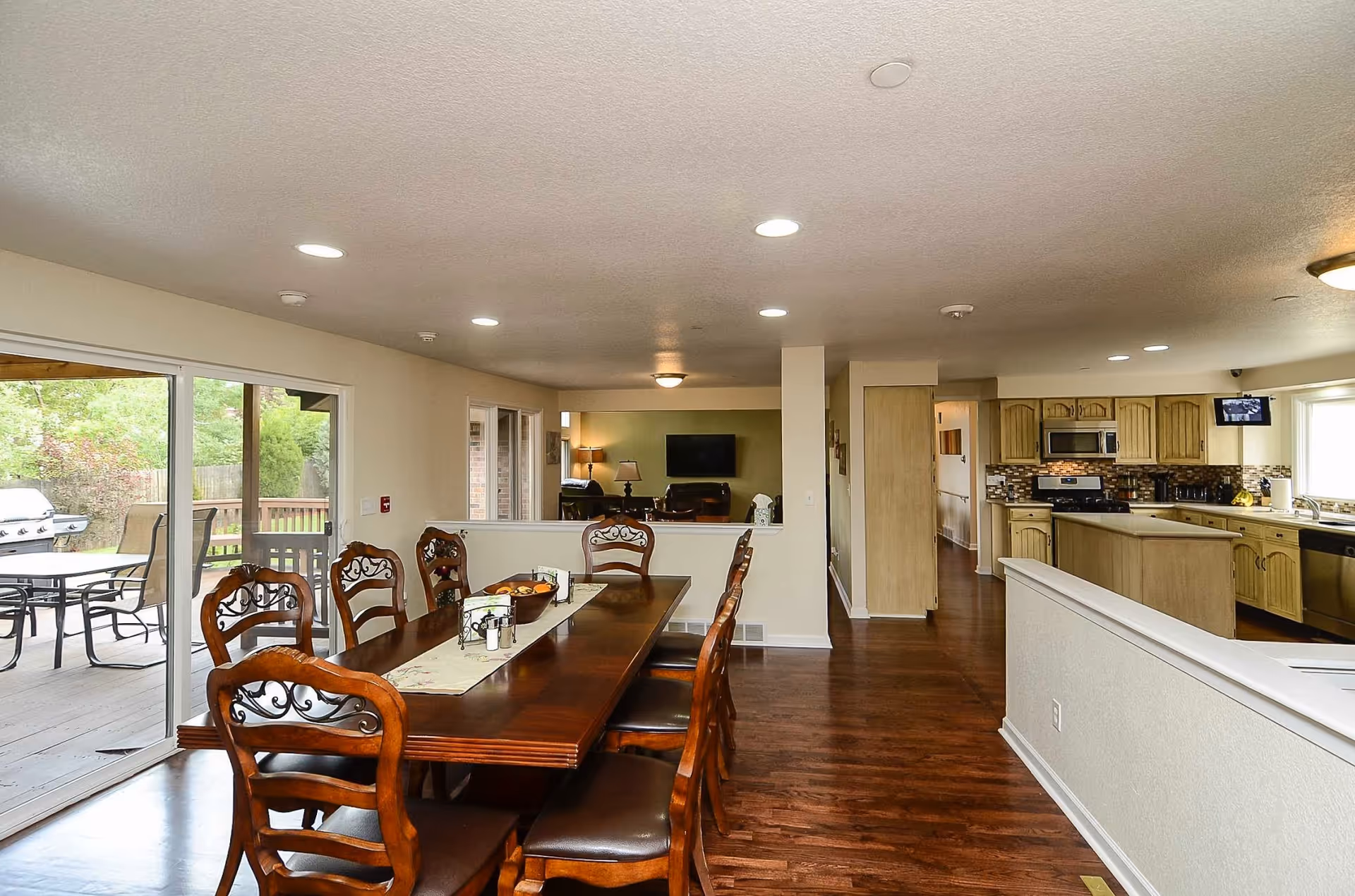 Open dining area with a long wooden table and chairs next to a kitchen and sliding glass doors leading to a patio.