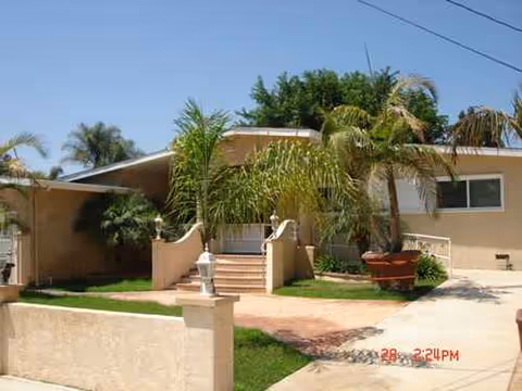 Single-story beige senior home with stairs, palm trees, and a small front yard entryway.