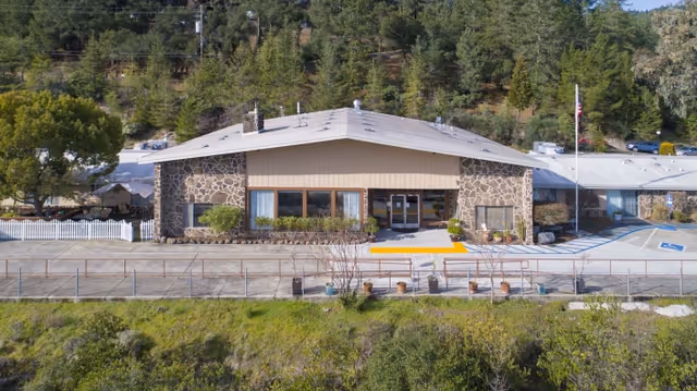 Front exterior view of Cloverdale Healthcare Center, a single-story building with stone and beige siding, surrounded by trees and greenery with a parking area including handicap spaces visible on the right.