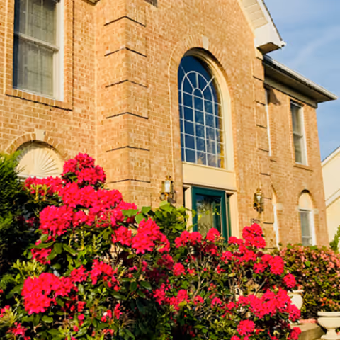 Brick senior living facility exterior with arched window and pink flowering bushes