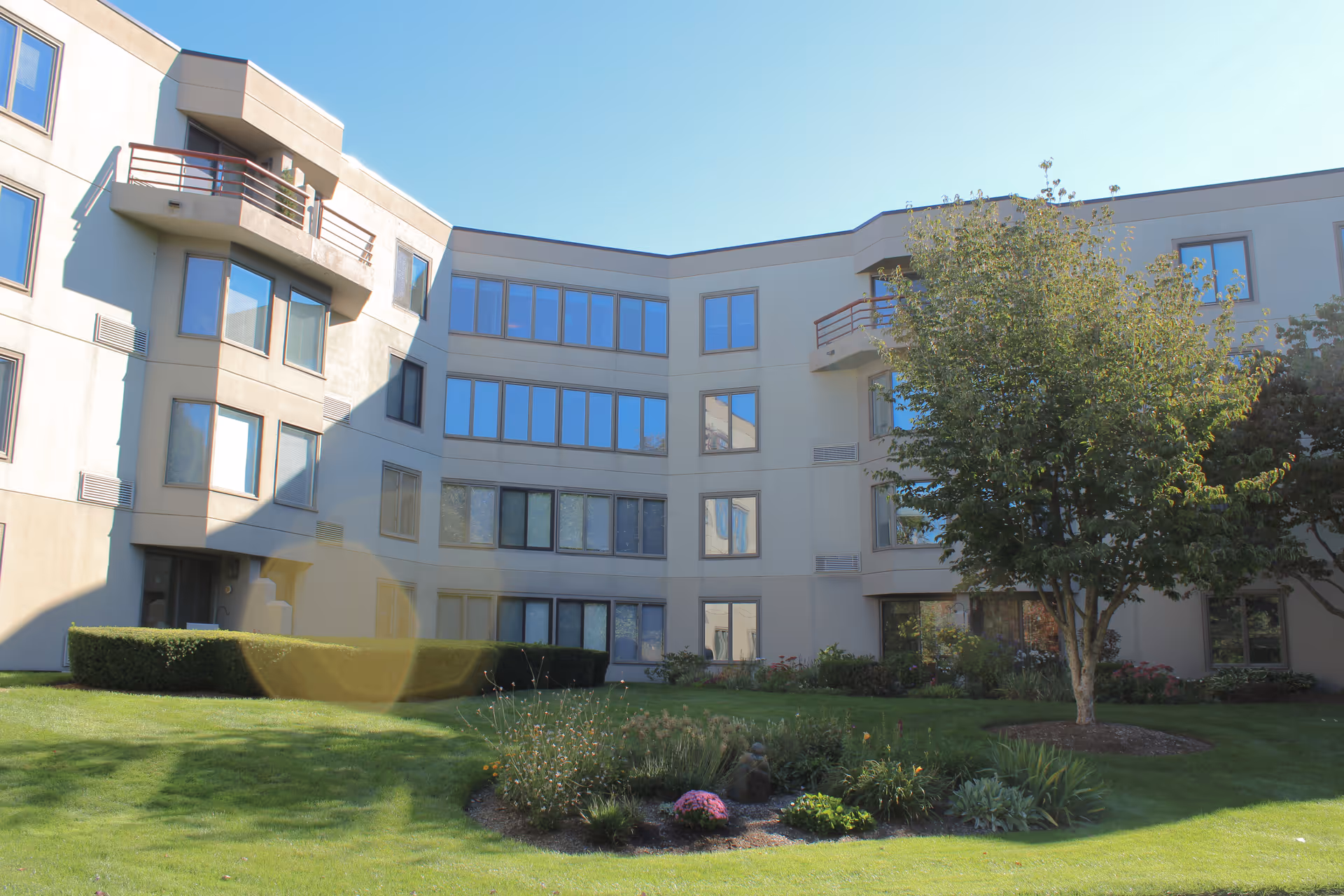 Courtyard and landscaped lawn in front of a three-story retirement community building with balconies and many windows.