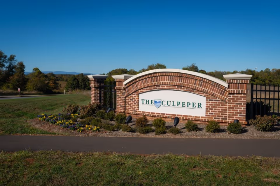 A brick entrance sign for The Culpeper with a landscaped flower bed in front and a clear blue sky in the background.