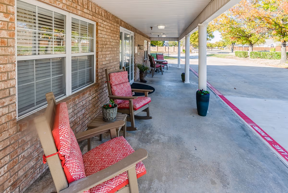 Covered front porch with red-cushioned chairs along the entrance walkway of a brick building.