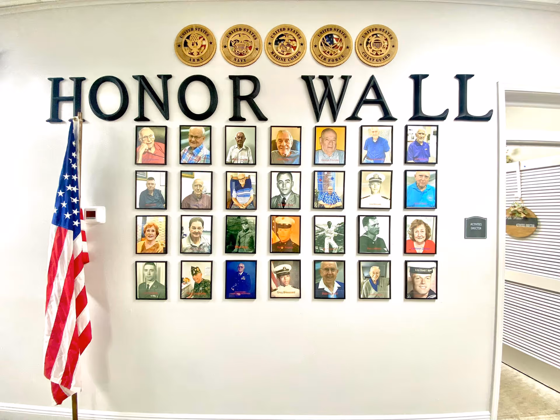 Indoor honor wall displaying framed portraits beneath large letters reading 'HONOR WALL' with an American flag beside it.