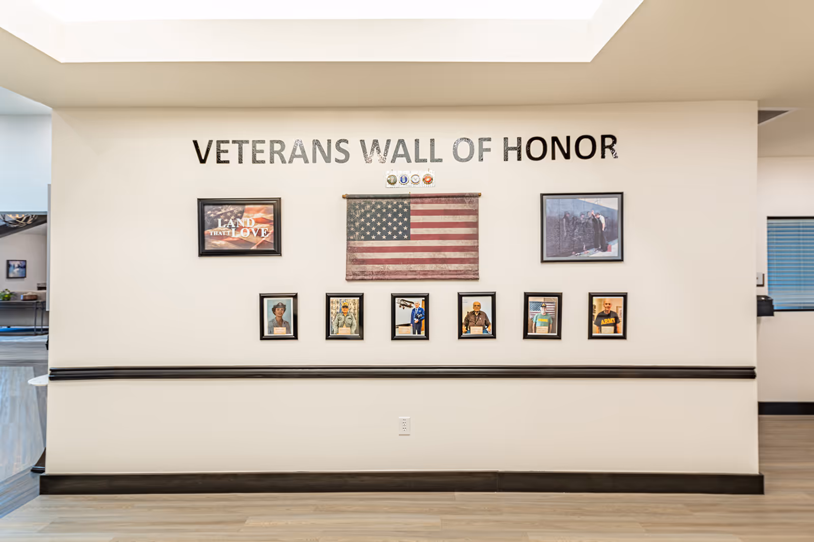 A Veterans Wall of Honor display on a white interior wall featuring an American flag and several framed photos and plaques.