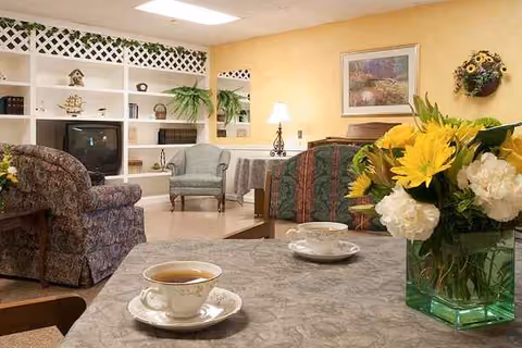 Cozy senior living lounge with seating, flowers, and a tea cup on the table.