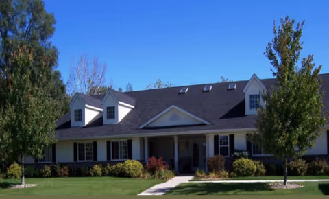 Front view of Avonlea Cottage of Quad Cities with lawn, trees, and entrance walkway.