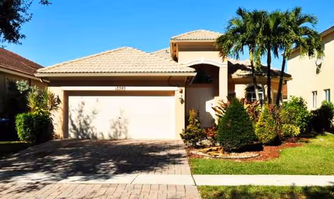 A beige residential-style building front with a garage, palm trees, and landscaping.