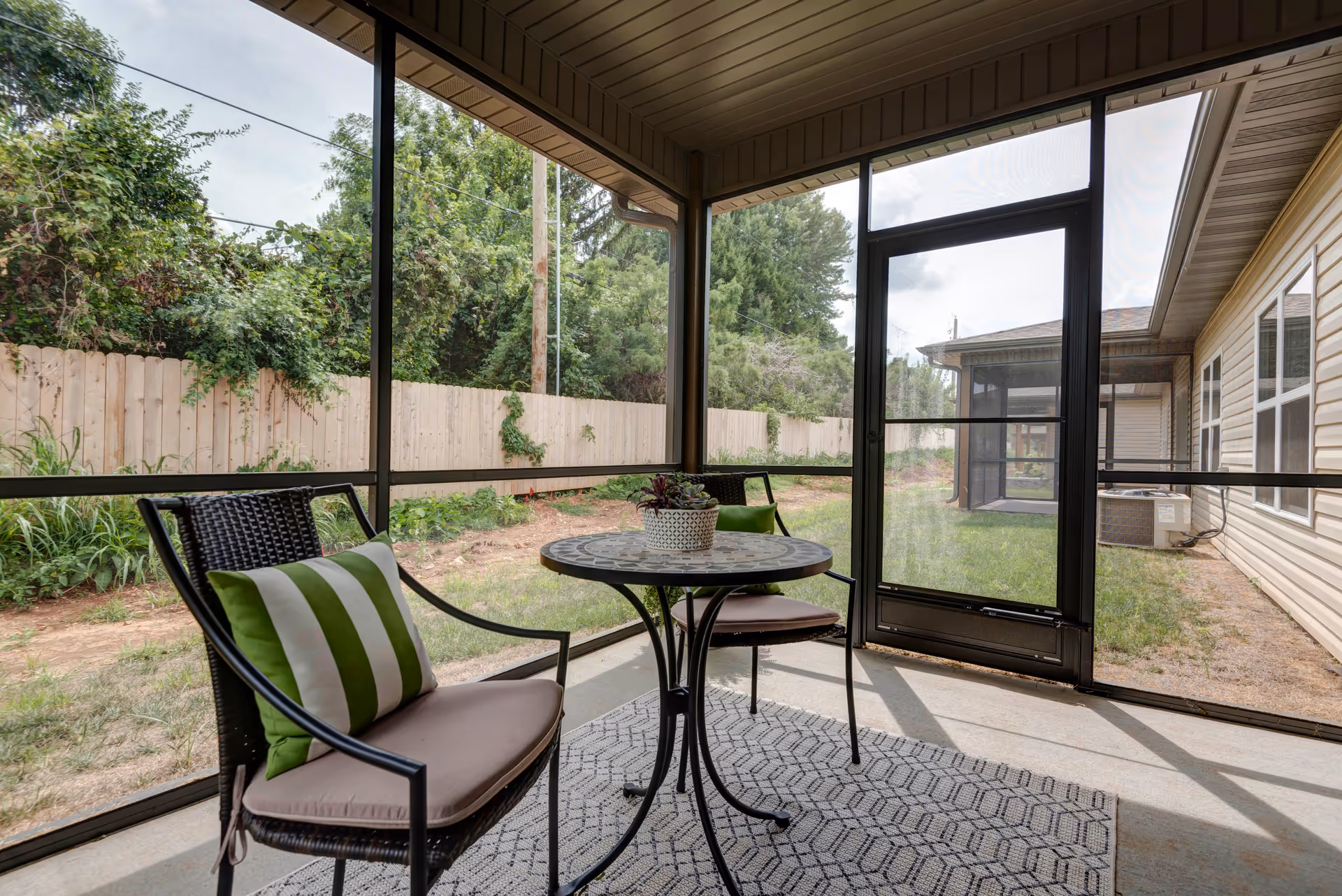 Screened-in patio with a small round table and two chairs overlooking a fenced backyard.