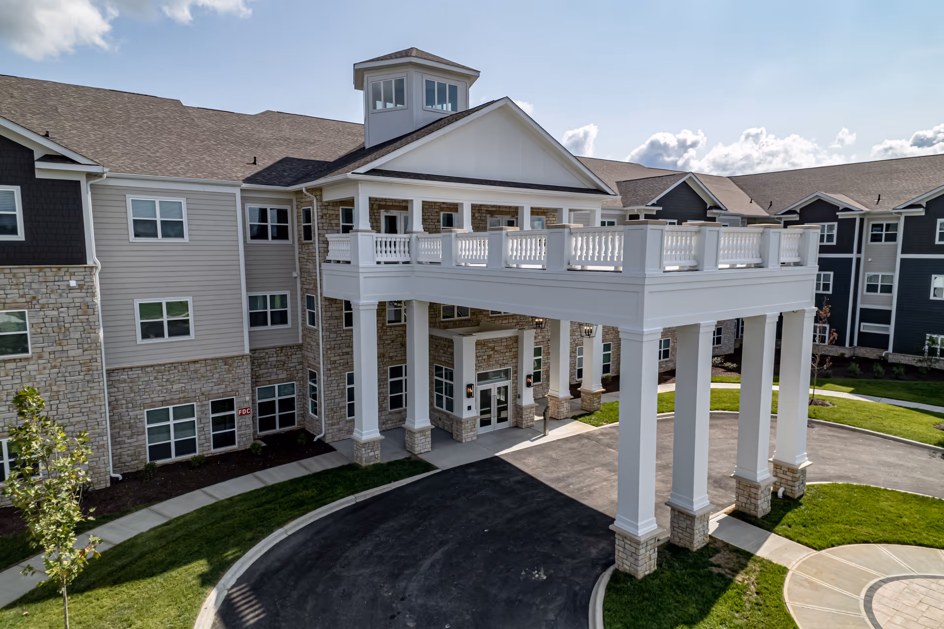 Front entrance of Bridgepointe Gardens showing a multi-story building with a large white columned porte-cochere and stone-and-siding facade.