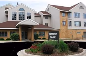 Exterior view of a multi-story senior living facility named Pinecrest Village with a covered entrance, large windows, and landscaped garden beds in front.