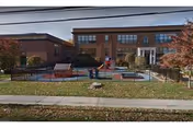 Brick two-story building with a fenced outdoor play area and sidewalk in front.