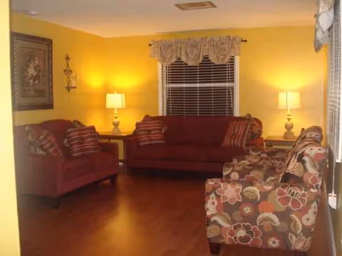 Cozy yellow living room in a senior living facility with red couches and lamps.