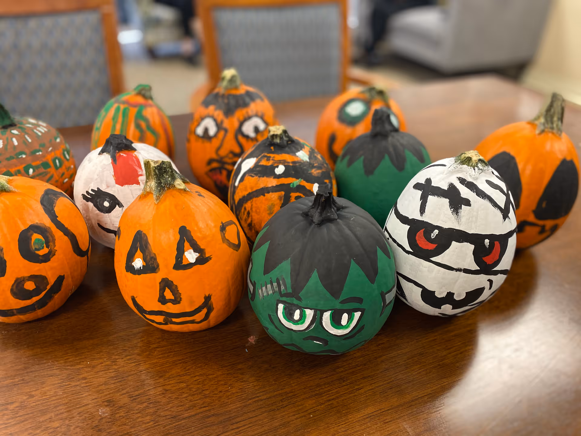 A group of small painted decorative pumpkins with various faces arranged on a wooden table.