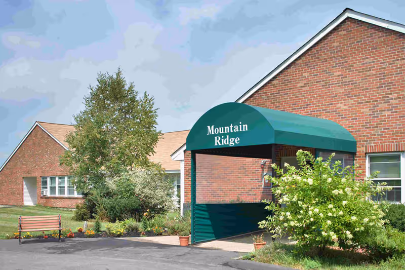 Front exterior of a brick building with a green awning reading "Mountain Ridge" over the entrance and surrounding landscaping.
