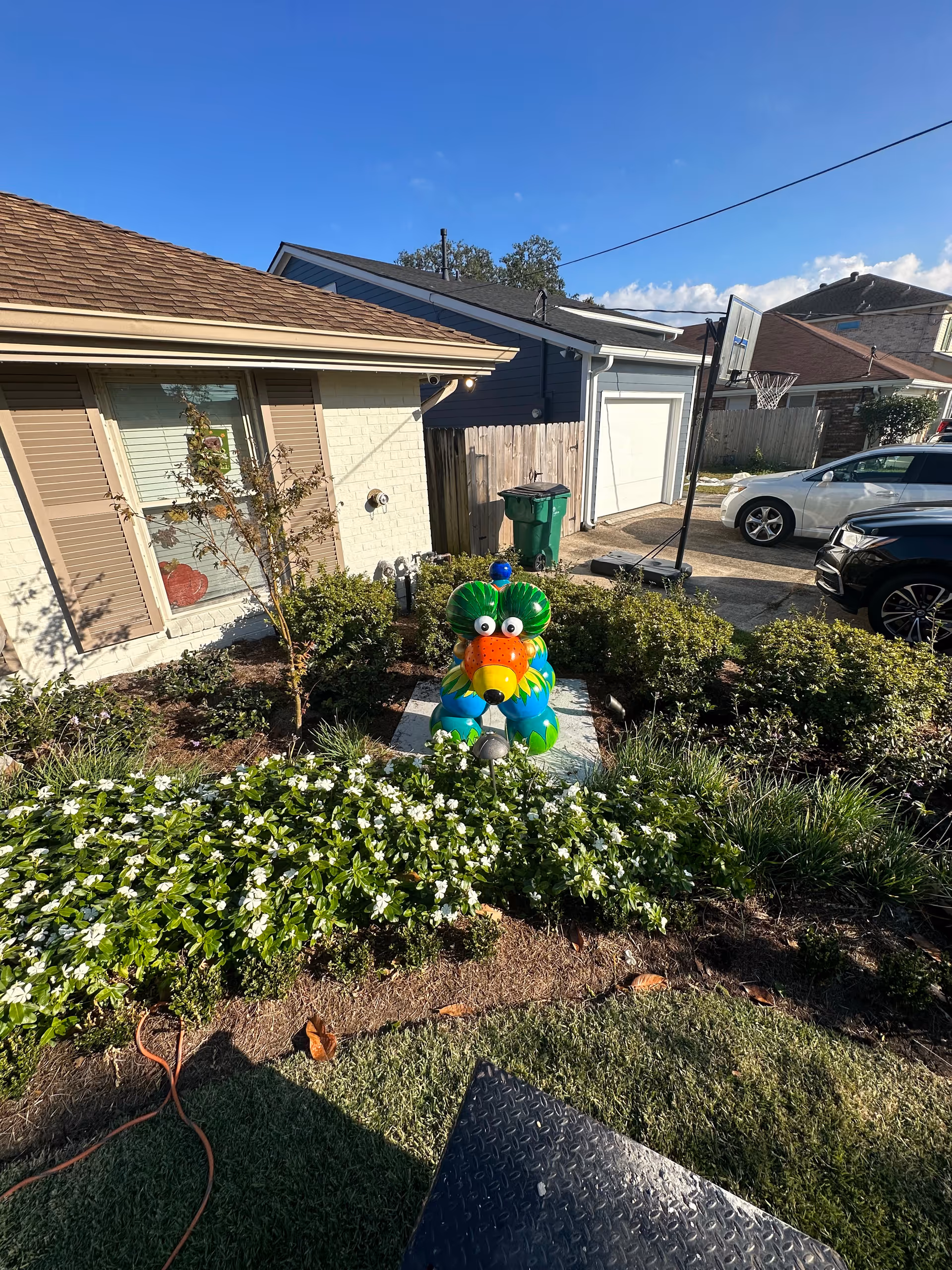 Front yard of a house with flower beds and a colorful decorative animal statue near a driveway and garage.