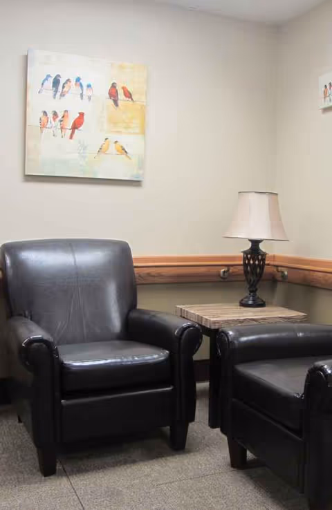 Two black leather armchairs with a side table and lamp in a beige-walled lounge.