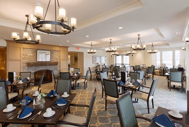 Spacious dining room with multiple set tables, chandeliers, and a stone fireplace.