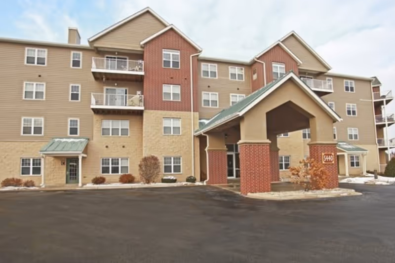 Front exterior of a multi-story apartment-style senior living building with a covered porte-cochère entrance and balconies.