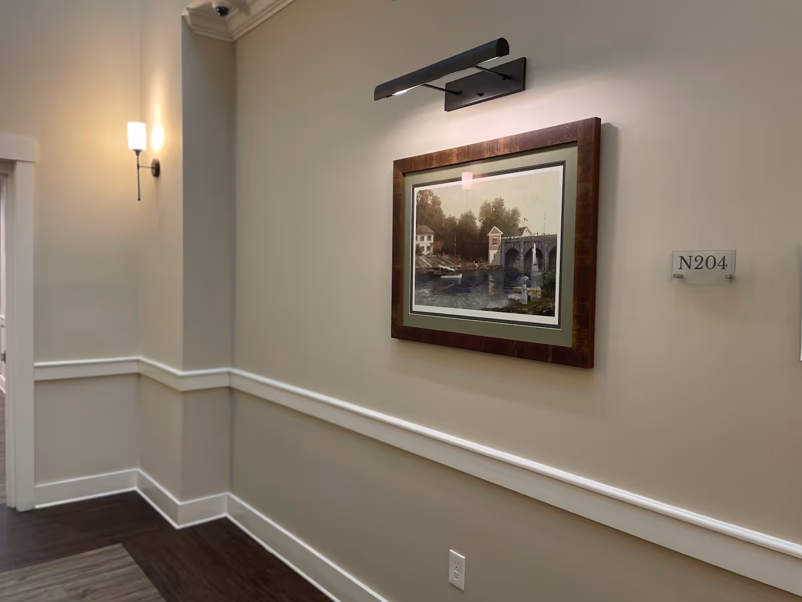 Interior hallway with a framed painting, wall sconce lighting, and a room number sign reading N204.