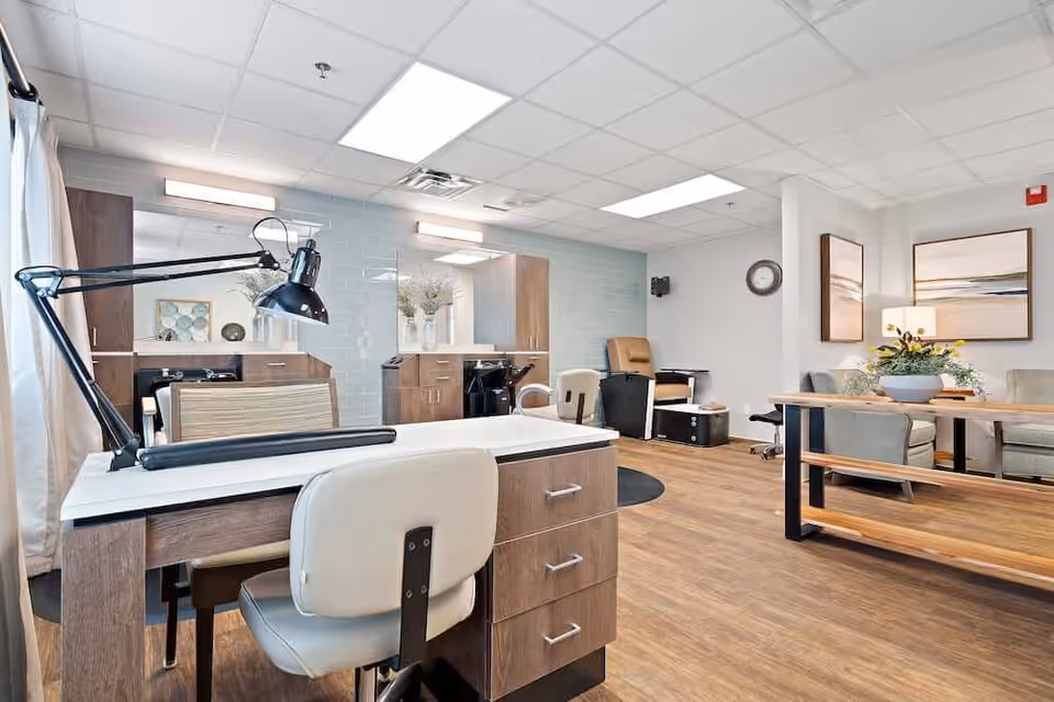 Bright, modern salon-style common room with a manicure table, styling chairs, hair-wash stations, and a seating area.