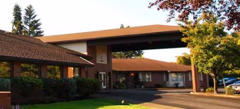 Brick senior living facility with a covered entrance and surrounding trees.