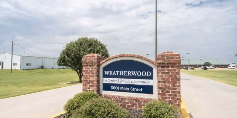 Weatherwood senior living sign on brick entrance structure beside a driveway.