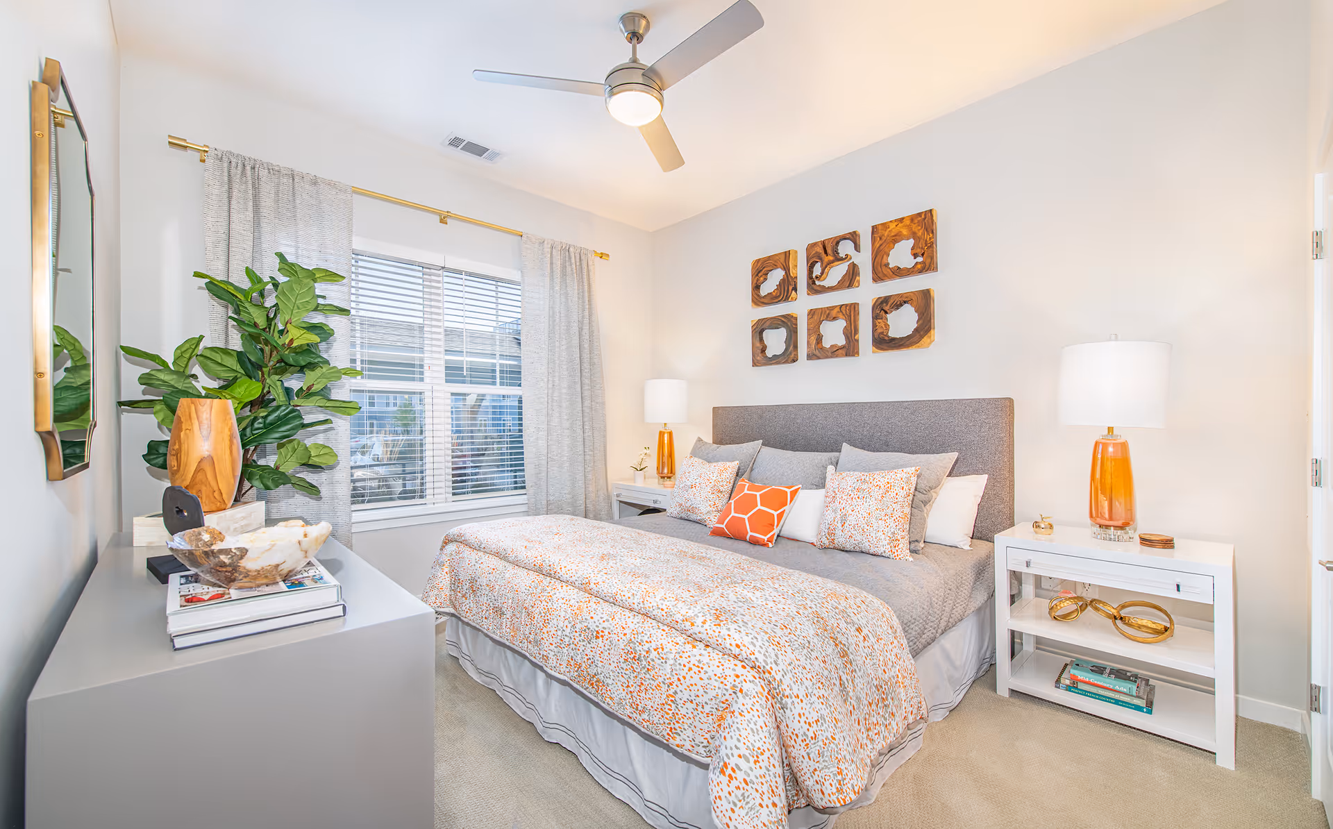 Bright modern bedroom with a large upholstered bed, patterned bedding, bedside tables, decorative wall art and a window with curtains.