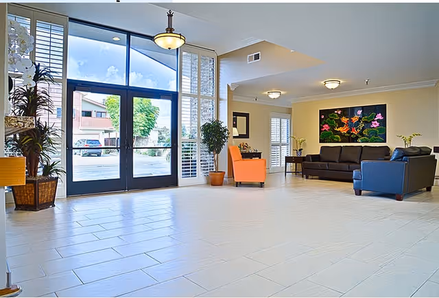 Bright, spacious lobby with large glass entrance doors, tiled floor, seating area, plants, and wall artwork.