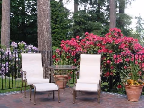 Two cushioned patio chairs with a small table on a brick outdoor patio surrounded by flowers.