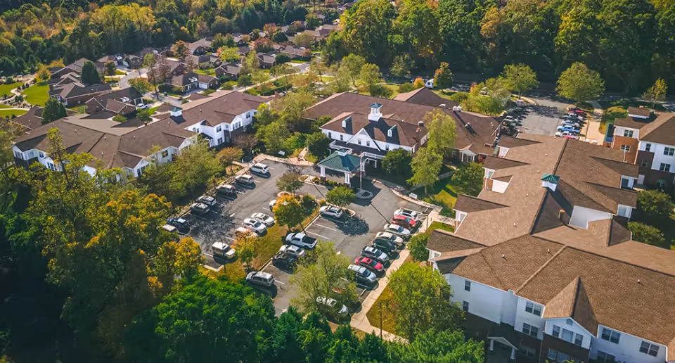 Aerial view of the Homestead Hills senior living campus showing multiple connected buildings, a central parking lot, and surrounding trees.