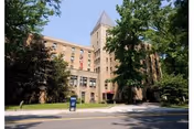 Brick senior living building with a tower, trees lining the sidewalk in front.