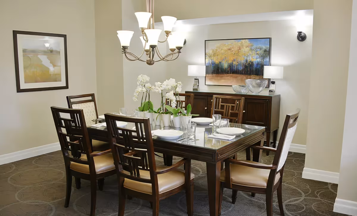 Formal dining room with a dark wood table set for six, a chandelier overhead, a floral centerpiece, and artwork on the walls.