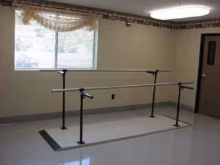 Interior rehab room with parallel bars for gait training, window, door, and ceiling light.