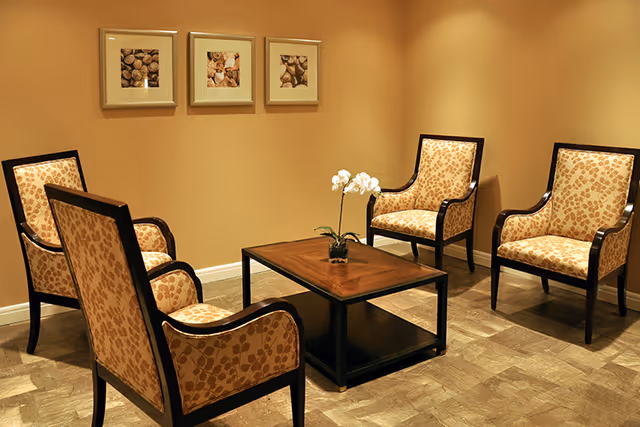 A small lounge with four patterned armchairs arranged around a wooden coffee table topped with a potted orchid and framed artwork on the wall.
