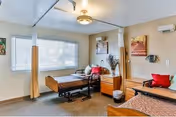 Two-bed patient bedroom with wooden hospital beds, a nightstand, window blinds, ceiling light and privacy curtains.