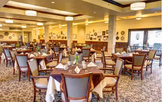 Spacious dining room with multiple round tables set with tablecloths, chairs, and place settings under warm lighting.