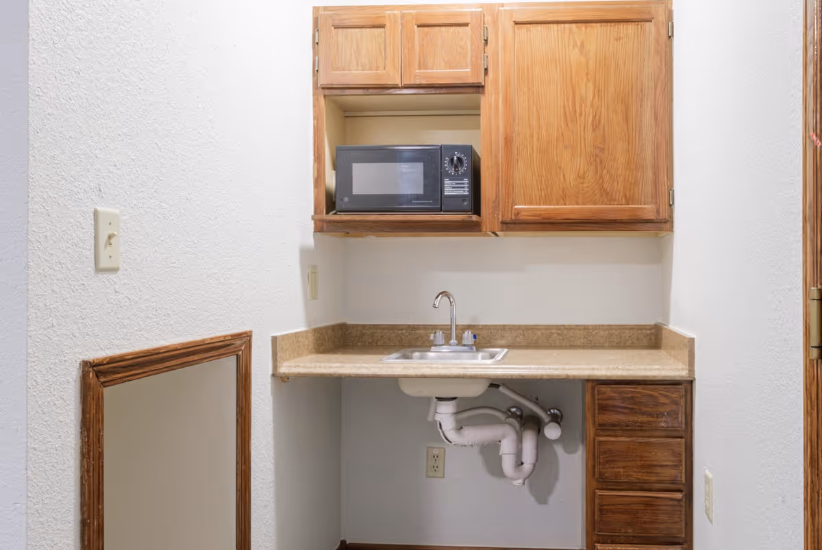 Small kitchenette with a sink, countertop, wooden cabinets and a microwave.