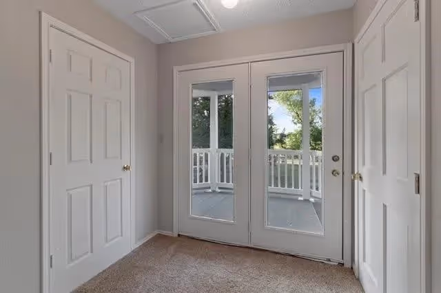 Carpeted interior room with double glass doors leading to a small balcony and closets on either side.