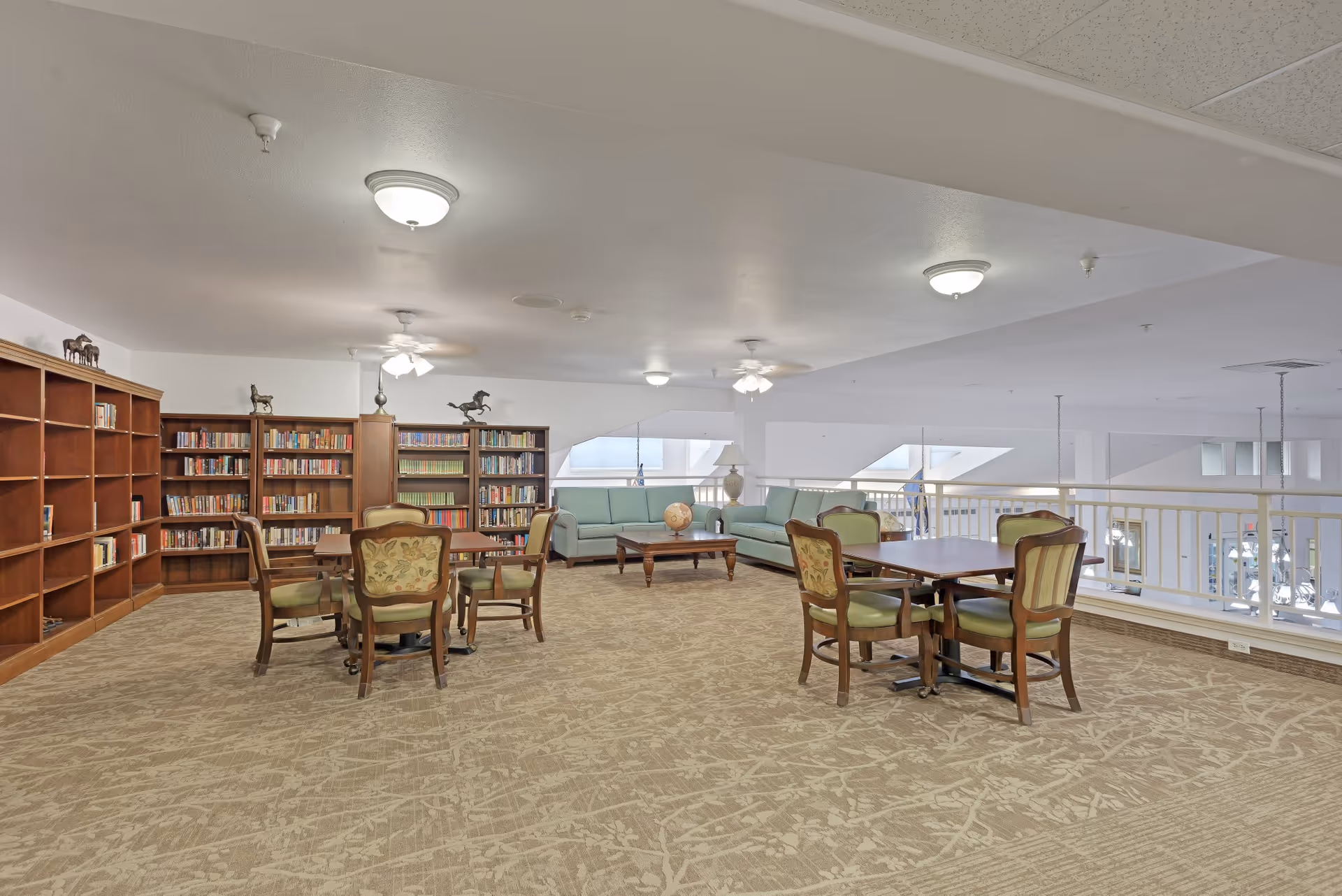 Open upper-level community lounge with bookshelves, tables and chairs, and sofas overlooking the lower level.