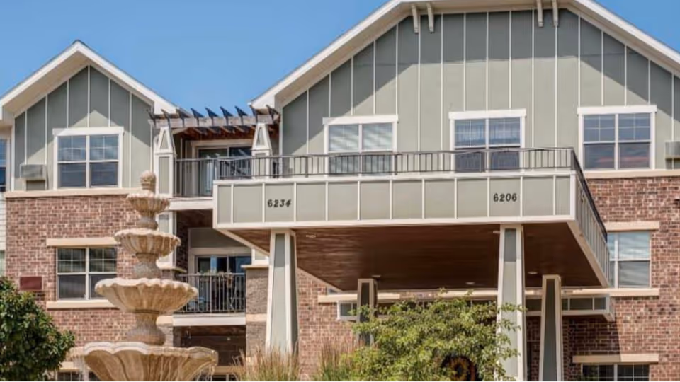 Front exterior of a multi-story brick-and-siding building with balconies and a tiered fountain in the foreground.