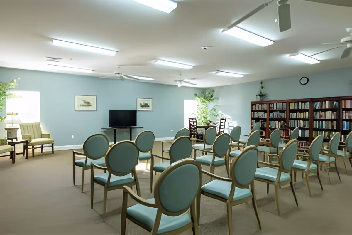 Spacious common room with rows of teal-upholstered chairs facing a TV and bookshelves.